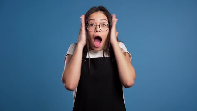 Portrait of cute asian girl shocked, saying WOW. Pretty woman with perfect make-up, stylish outfit pleasantly surprised to camera over blue background. 