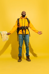 Happy laughting. Portrait of a cheerful young african-american tourist guy with bag and binoculars isolated on yellow studio background. Preparing for traveling. Resort, human emotions, vacation.