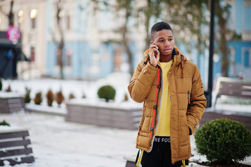 African man wear on orange jacket at winter cold weather posed outdoor with mobile phone.