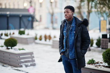 African man wear on jacket at cold winter weather posed outdoor with headphones on ears.