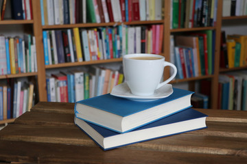 Kaffee, Cappuccino in Tasse mit Buch vor Bücherregal