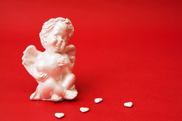 Closeup gypsum angel with a heart on a red background. Decorative Cupid for Valentine's Day.