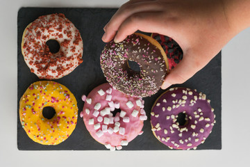 Caucasian boy getting donuts of various flavors with shavings on slate surface. Snack concept.