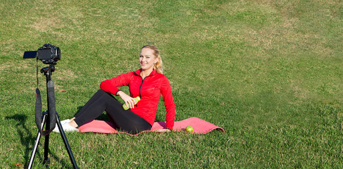 sporty dressed young woman is doing vlog video while doing sports on grass
