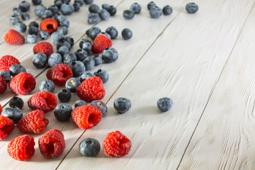 Raspberries and blueberries scattered on the white wooden floor