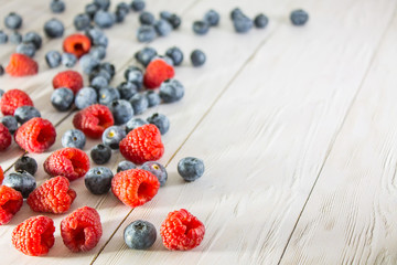 Raspberries and blueberries scattered on the white wooden floor