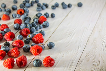 Raspberries and blueberries scattered on the white wooden floor