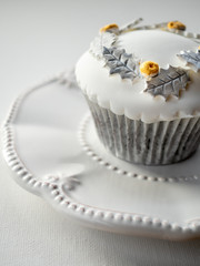 White cupcake with gold and silver decoration on white plate and  white background. Close up.