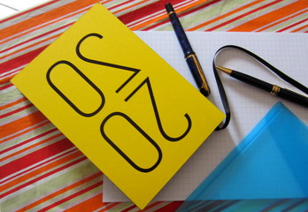 Yellow notebook organizer for 2020, two pens, a plastic blue file for documents and a checkered brulion on a colourful striped tablecloth