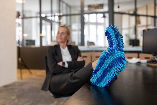 Mature businesswoman with feet on desk wearing cleansing slippers in office