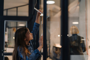 Girl drawing on glass pane in office