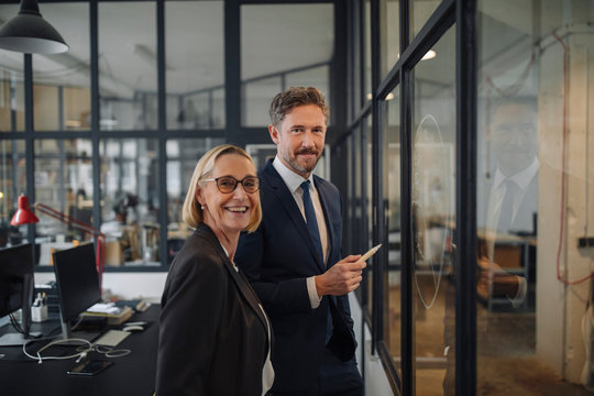 Smiling businessman and businesswoman standing at drawing on glass pane in office