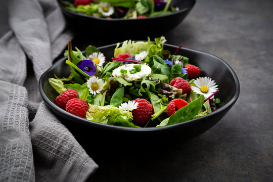Bowl of fresh salad with arugula, spinach, chard, oak leaf, lollo rosso lettuce, corn salad, raspberries, cream cheese, chive and edible flowers