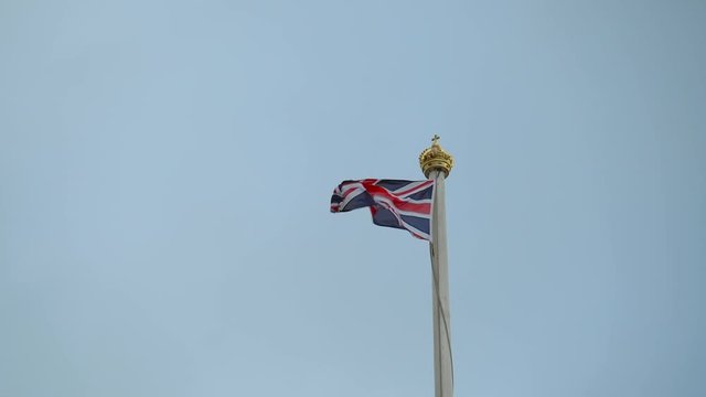British flag or union jack flying on a flag pole against sky. England flag waving on the top. Flag pole with krown and British flag Union Jack in Buckingham Palace. Britain flag in rainy weather.