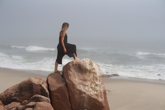 Woman standing on a rock looking to the ocean, Cape Cross, Namibia