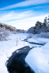 Stream running through a snow covered Wisconsin forest with snow covering the trees in January