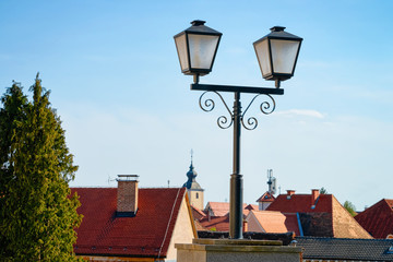 Fototapeta na wymiar Cityscape with street lantern and house roofs with Our Lady of the Seven Sorrows Church in Old center in Slovenska Bistrica near Maribor in Slovenia. South Styria in Slovenija. Light in Slovenian town