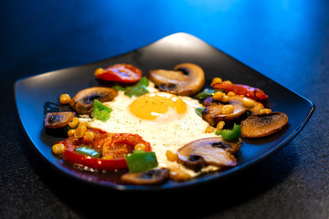 Freshly fried scrambled eggs with vegetables on a black plate