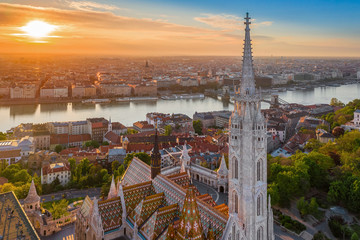 Budapest, Hungary - Aerial drone view of the beautiful Matthias Church at Castle district with a warm summer sunrise. Fisherman's Bastion and Szechenyi Chain bridge at background - obrazy, fototapety, plakaty