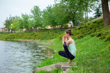 A young sports girl practices yoga on a green lawn by the river, yoga assans posture. Meditation and unity with nature