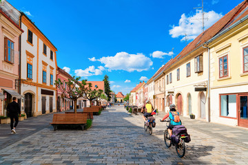 Family on bicycles in Street with benches in Old city in Varazdin in Croatia. Cityscape with tourists in famous Croatian town in Europe in summer