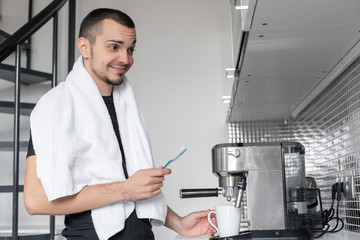A young guy is going to work in the morning. Brushes teeth near a coffee machine while waiting for a cup of coffee