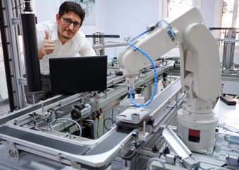 Close-up of an engineer who is with laptop, programming smart factory automation looking at camera and making OK sign. Industry 4.0 concept; artificial intelligence in smart factory.