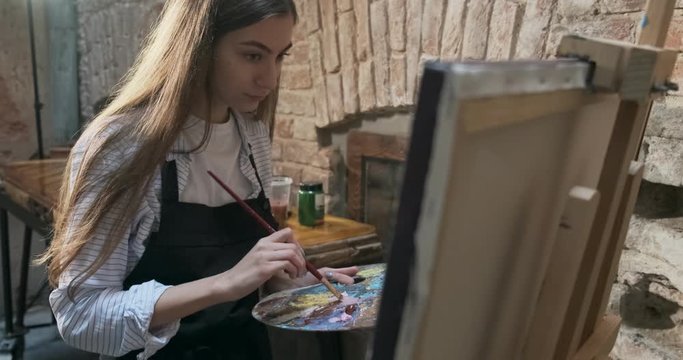 Talented innovative pretty Female Artist Draws with brush on the Canvas. Contemporary young woman painter creating abstract picture. Attractive girl creates modern art painting