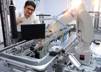 Close-up of an engineer who is with laptop, programming smart factory automation looking at camera and making OK sign. Industry 4.0 concept; artificial intelligence in smart factory.