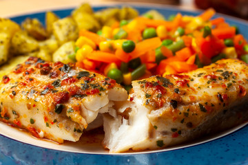 Colorful fish chargrill with tomatos and herbs on a plate with mixed vegetables and potatos