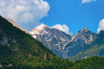 Fototapeta na wymiar Julian Alps mountains on Bohinj Lake in Slovenia. Alpine Nature in Slovenija. View of green forest. Beautiful landscape in summer. Travel destination. Scenic background with blue sky and white clouds