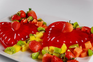 Raspberry heart gelatin decorated with chopped fruit on white plate.