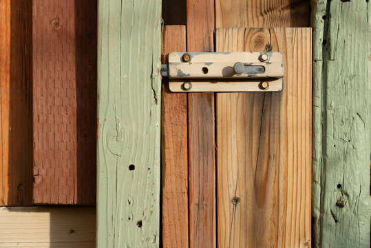 A close up deail of a locked gate latch on a rustic fence made from a mismatched mix of multicolored painted or stained wood