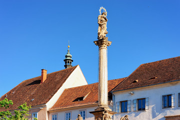 Fototapeta na wymiar Main square with Plague Column in small spa town on thermal springs Bad Radkersburg in Styria in Austria. Street view in Austrian city. Building architecture. Blue sky