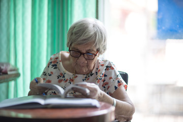 Asian old woman Sitting and writing on the table by the glass window in the house To train the brain and memory Not to be forgotten