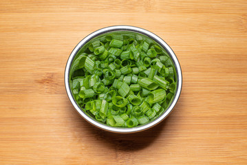 Chopped Chive garnish, in steel bowl on wooden board, top down with drop shadow.