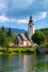 Scenery of Church of St John Baptist on Bohinj Lake in Slovenia. Nature in Slovenija. View of blue sky with clouds. Beautiful landscape in summer. Alpine Travel destination. Julian Alps mountains