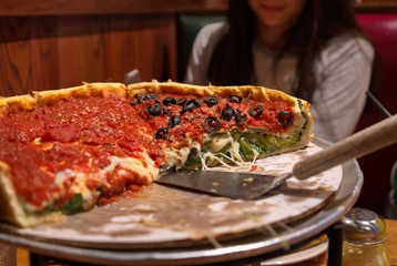 Half of a Chicago style deep dish pizza on a restaurant table with satisfied customer in the background..