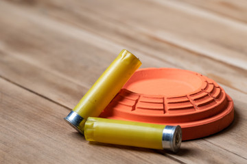 spent Shotgun shells laying next to a clay target on a wooden background. 