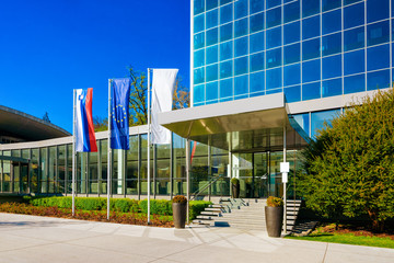 Street at Entrance into Medical center building at Old city in Rogaska Slatina in Slovenia in South Styria. Travel in Europe Slovenian luxury spa resort. Modern glass architecture exterior with flags. - obrazy, fototapety, plakaty