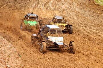 Three fast Buggy cars overtaking on muddy off road track, racing front view