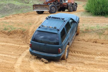 Big powered American 4x4 AWD car on off road track on bulldozer background, technical assistance rescue in dirt, rear view