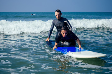 man instructor demonstrating how to stand up on surfboard to indian woman in surf class in Goa sea