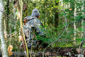 Obraz premium autumn hunter sits on log in a mixed forest, hunting and poaching, hunting for animals and game, opening hunting season