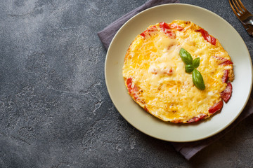 Omelet, scrambled eggs with tomatoes and cheese in a plate on a dark table.