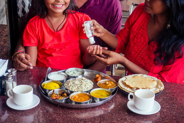 Father ,mother and little girl using wash hand sanitizer gel before eating in india cafe