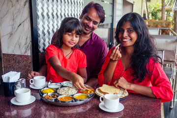 beautiful mother and happy father eating thali with daughter in cafe and drinking masala tea