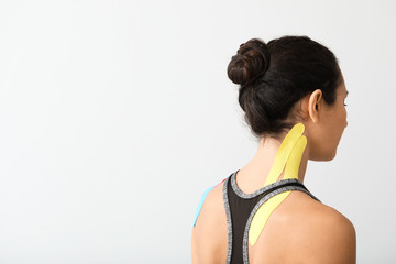 Fototapeta na wymiar Sporty woman with physio tape applied on neck against light background