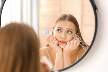 Thoughtful woman with contact lens case and eyeglasses near mirror