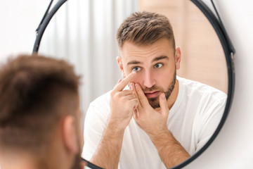 Fototapeta Young man putting in contact lenses near mirror obraz